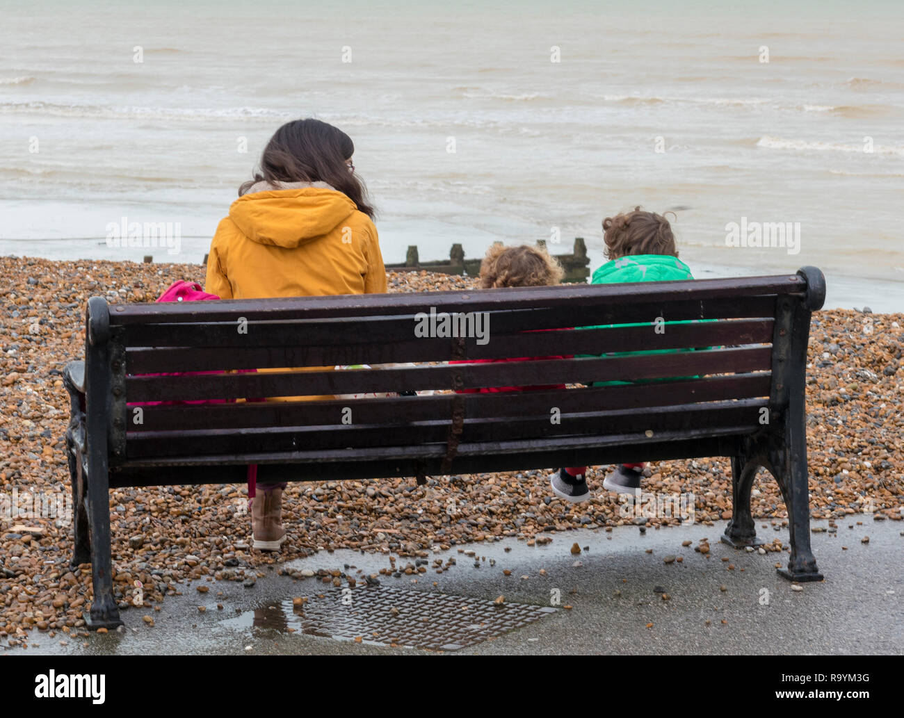 Mother And Two Small Children Sitting On A Wooden Bench At The