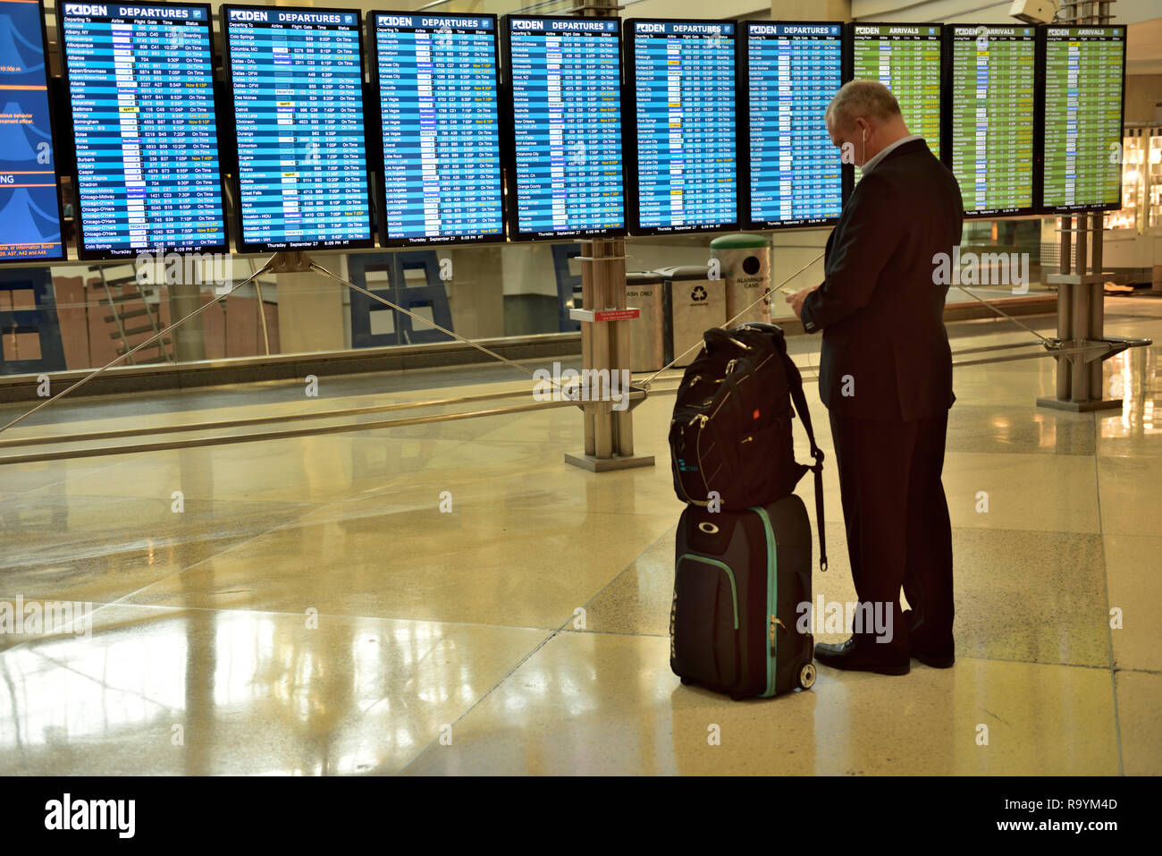 Man with suitcases checking the departure, arrivals board at airport, Denver International Airport (DEN), Colorado, USA Stock Photo