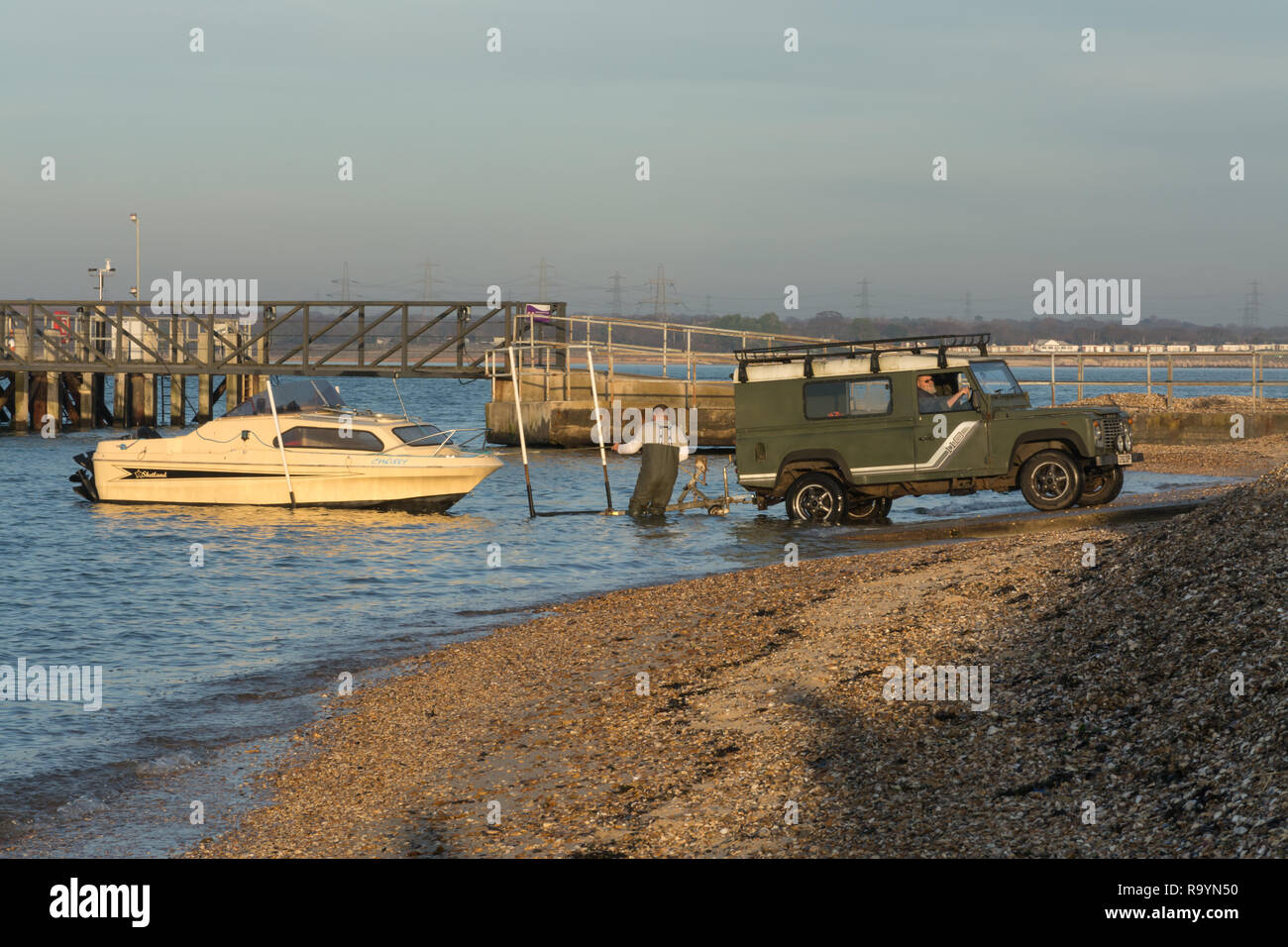 Two men launching a small boat down a ramp into the Solent using a four wheel drive vehicle, Hampshire, UK Stock Photo