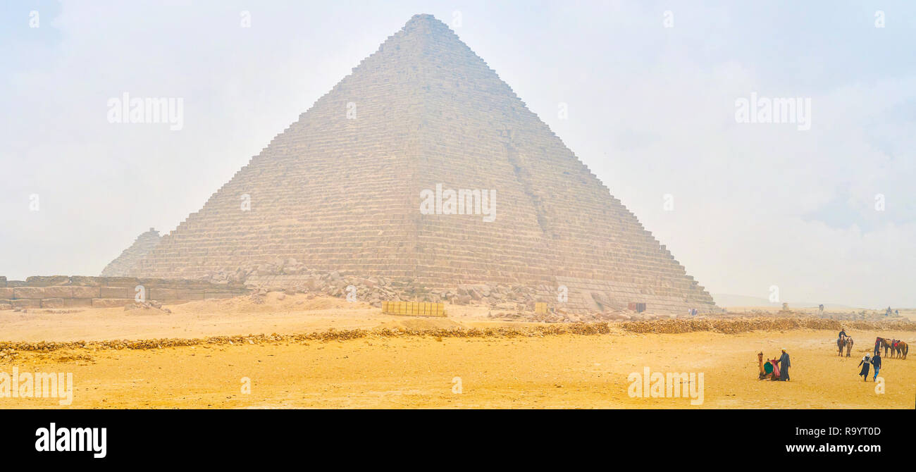 GIZA, EGYPT - DECEMBER 20, 2017: The beautiful view on Pyramid of Menkaure with walking tourists and cameleers offer camel riding service, on December Stock Photo