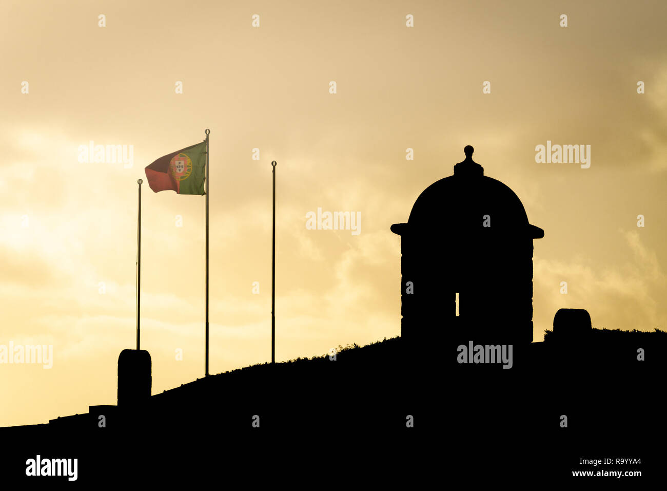 Silhouette of a small castle with a portuguese flag waving in the wind. Sunset. Copy space. Stock Photo
