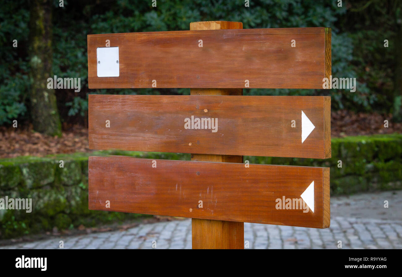 Side view of a wooden sign mockup with two signaling arrows and a white square. Green forest park background. Stock Photo