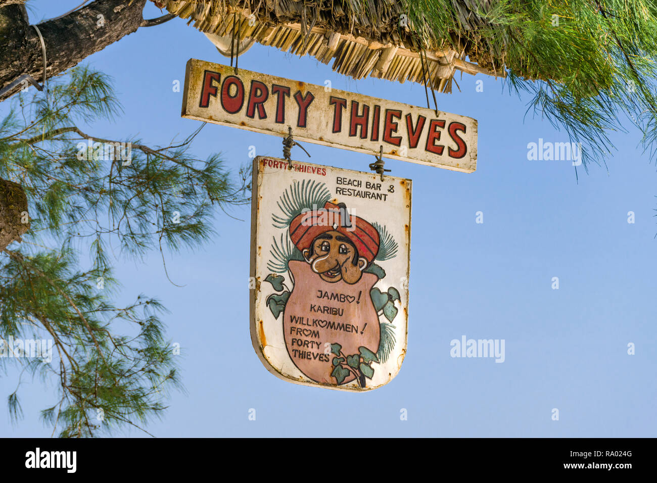 A sign for the Forty Thieves beach bar and restaurant hangs from a tree in the shade on a sunny blue sky day, Diani, Kenya Stock Photo