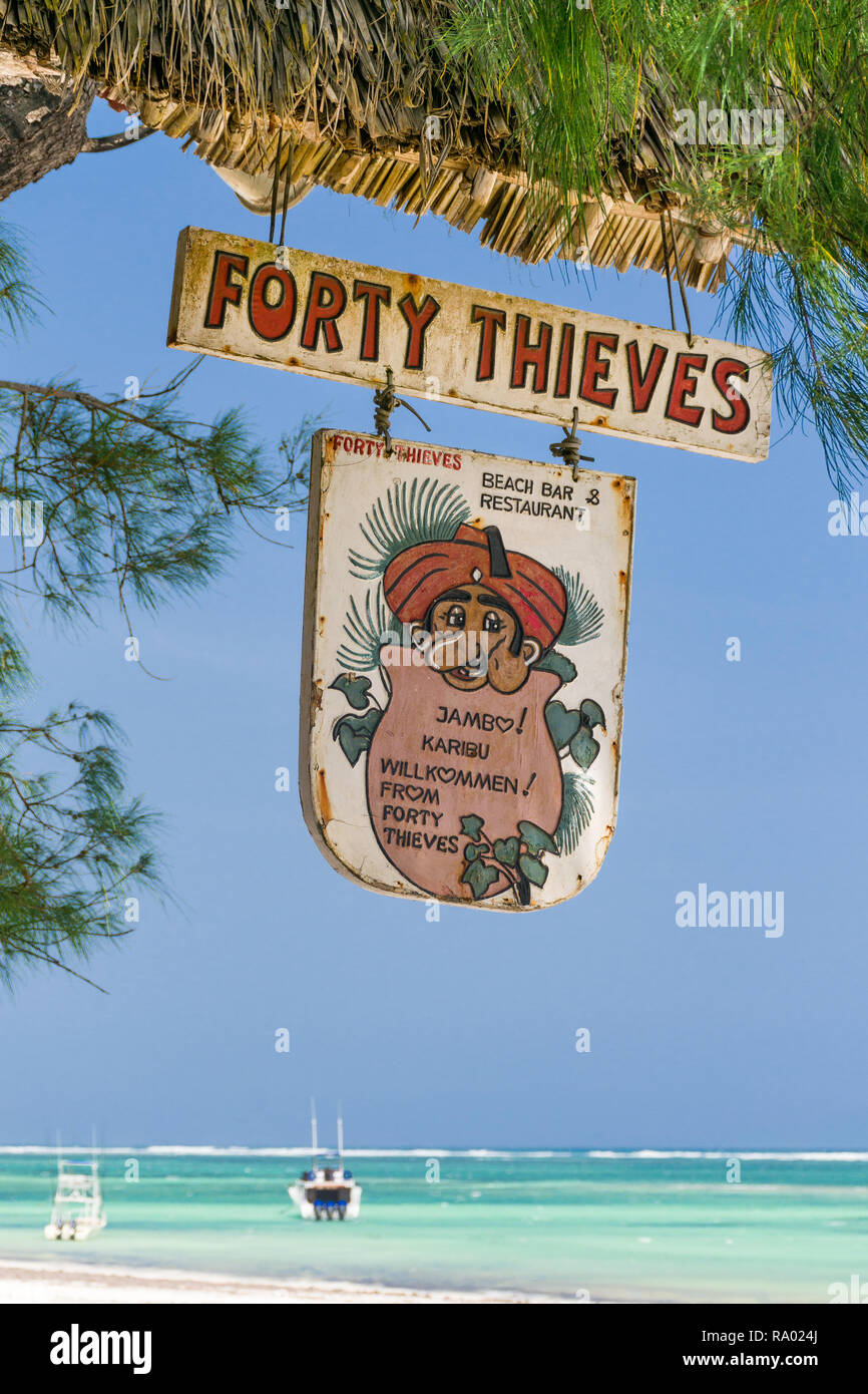 A sign for the Forty Thieves beach bar and restaurant hangs from a tree in the shade on a sunny blue sky day, Diani, Kenya Stock Photo