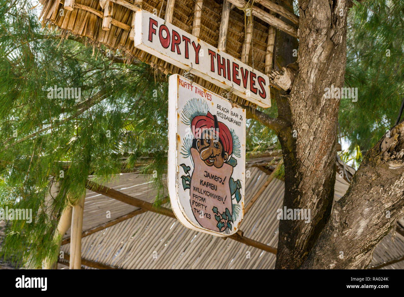 A sign for the Forty Thieves beach bar and restaurant hangs from a tree in the shade on a sunny day, Diani, Kenya Stock Photo