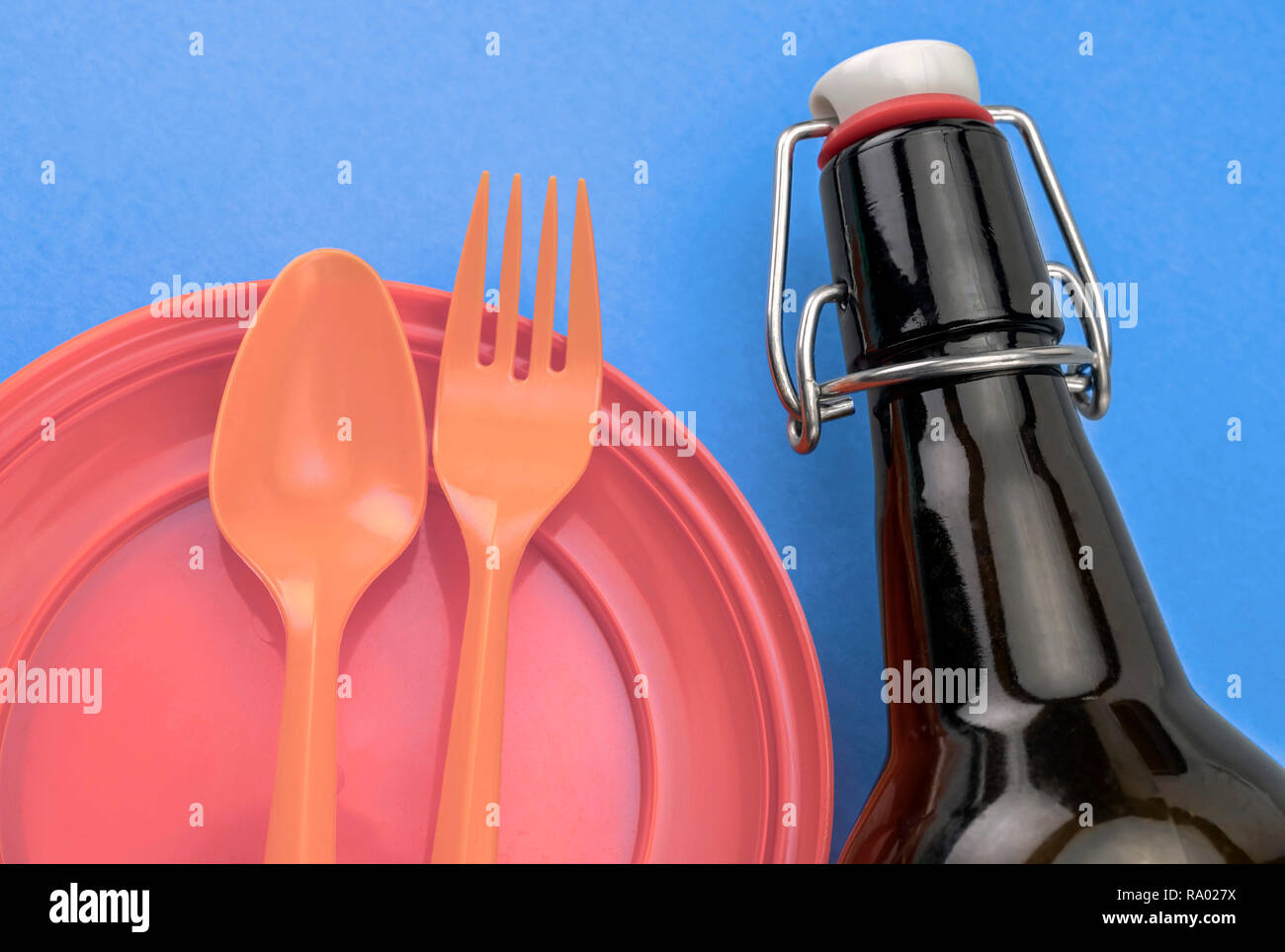 Orange dish and plastic cutlery next to a glass bottle, conceptual image Stock Photo