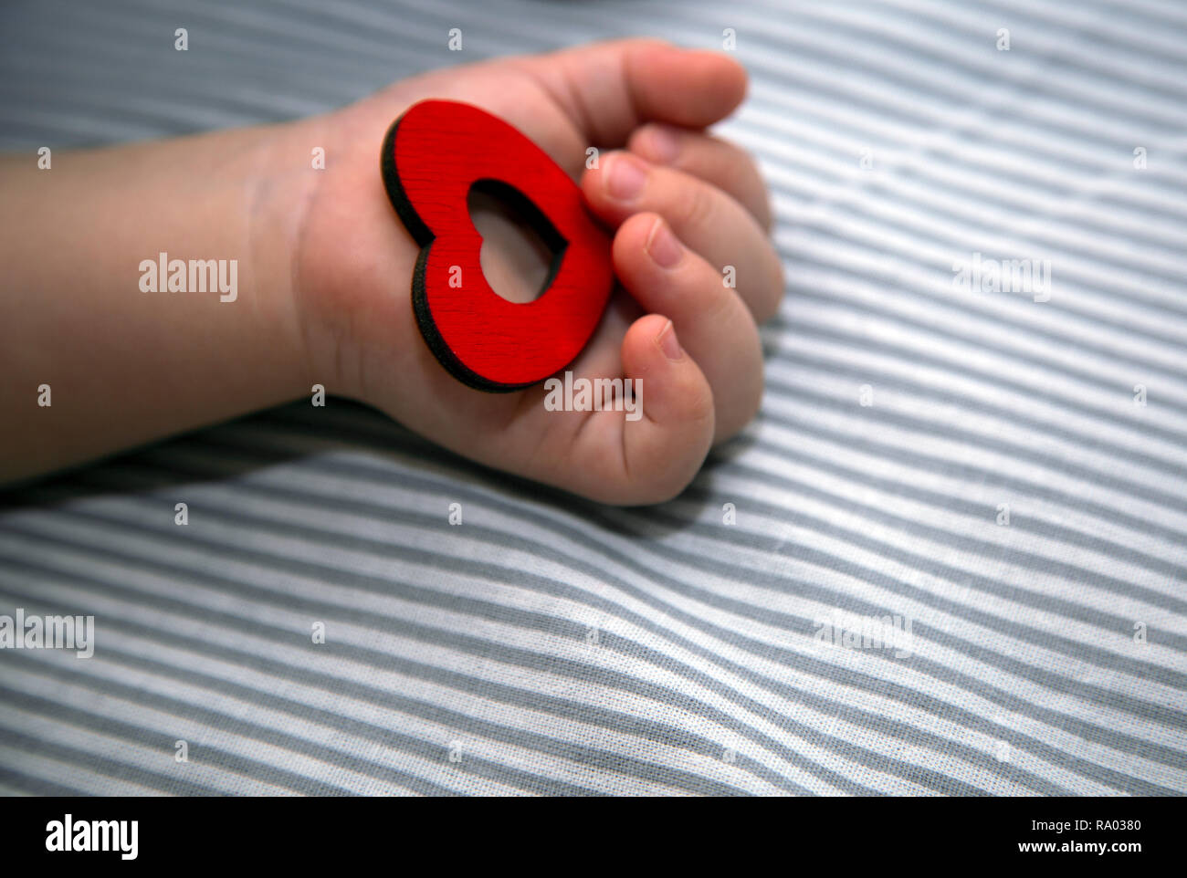 the newborn holds the red heart in his hand. Congratulations to the holiday Stock Photo