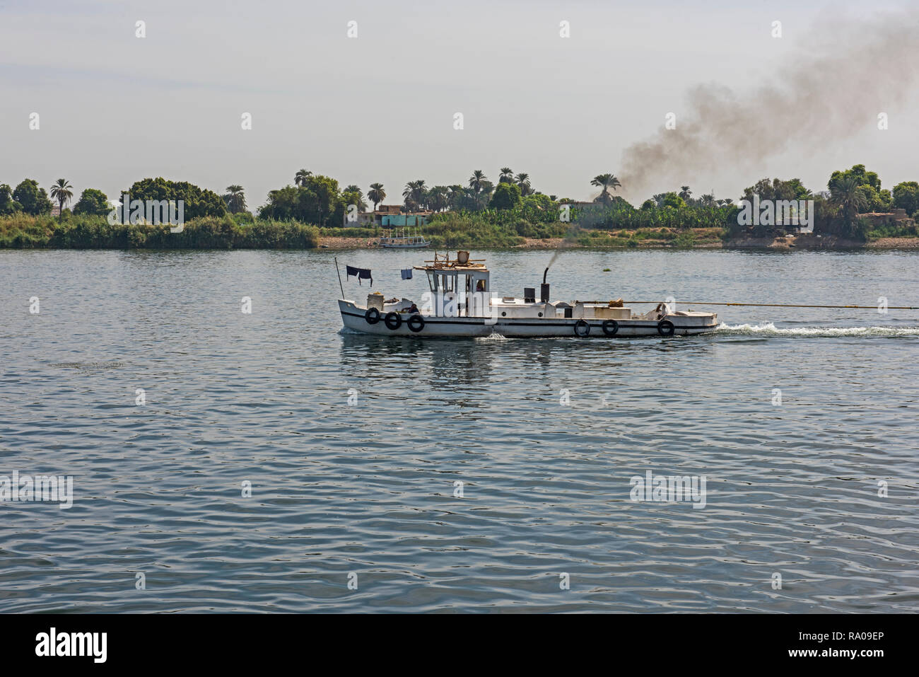 Small tug boat towing a barge on nile river in Egypt through rural countryside landscape with