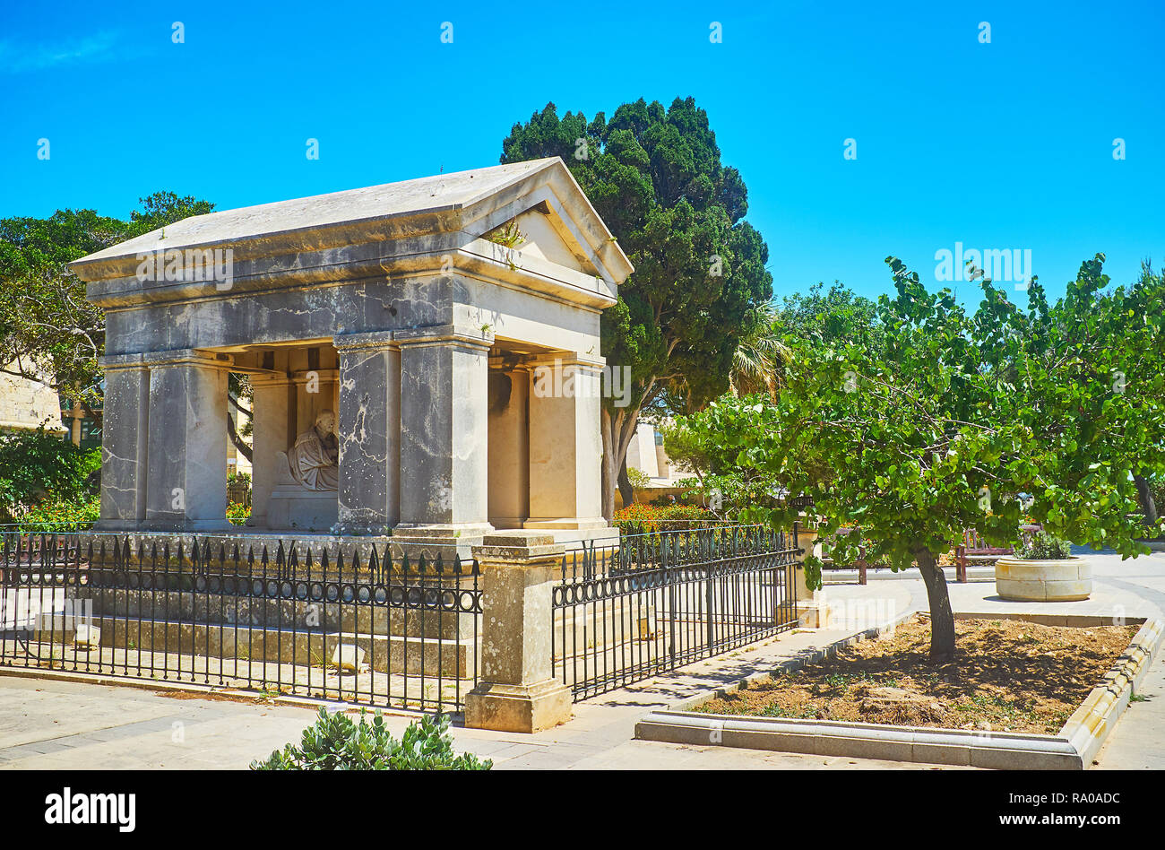 The lush greenery of Hastings Gardens surrounds the old stone memorial