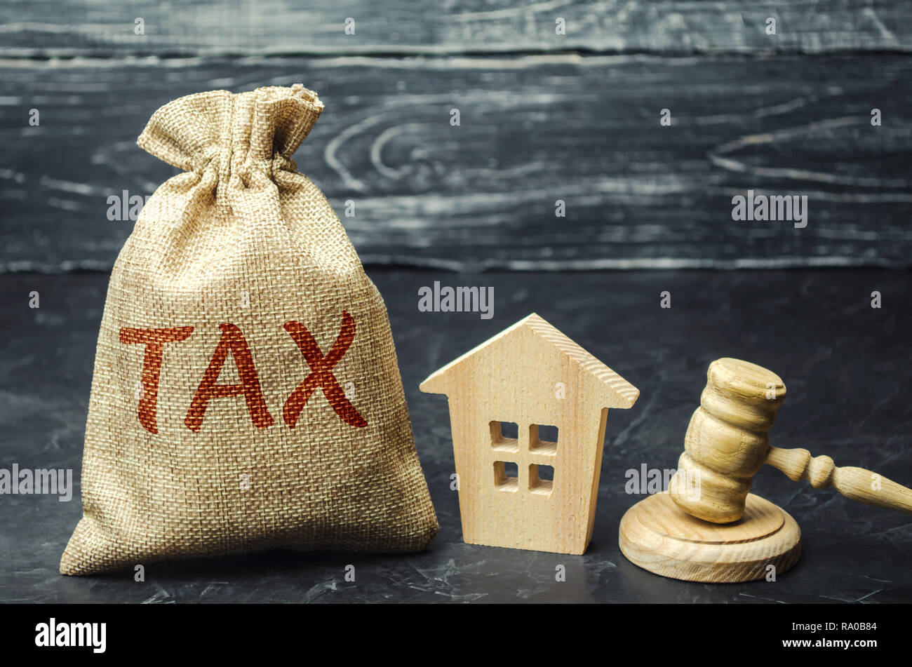 A bag with money and the word tax next to a wooden house. Taxes on real estate, payment. Penalty, arrears. Register of taxpayers for property. Law-abi Stock Photo
