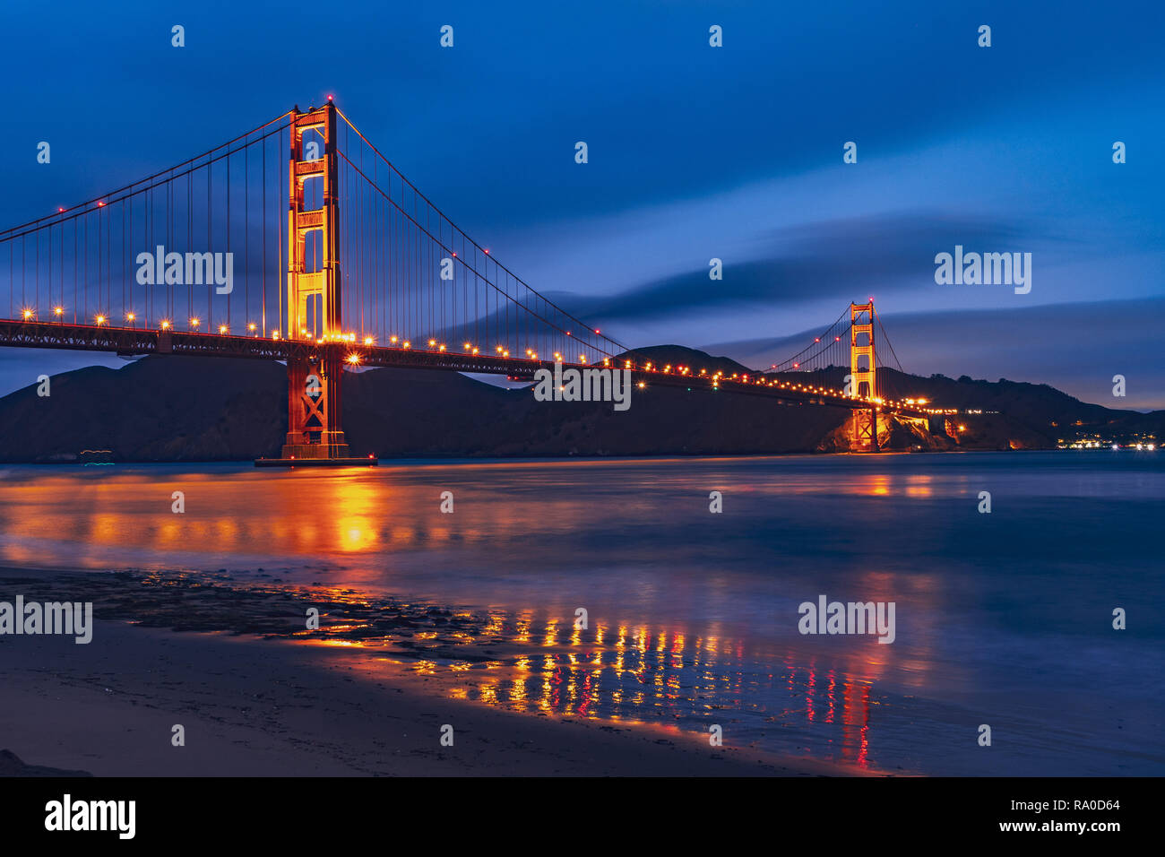 Nighttime view of Golden Gate Bridge reflected in the blurred water surface of San Francisco bay, dark blue sky background; California Stock Photo