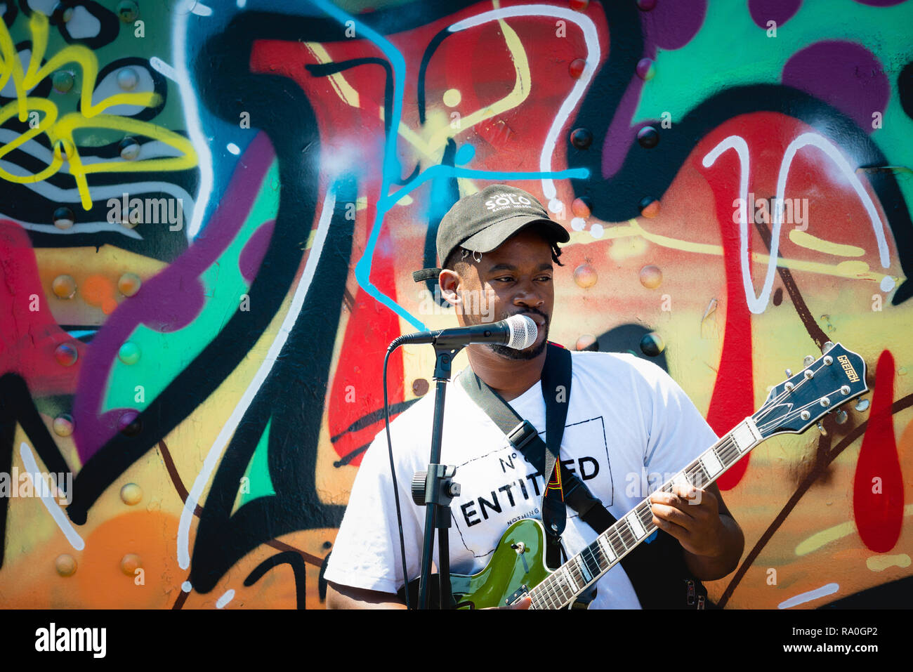 Busker performing in front of colourful street art at Brick Lane market ...