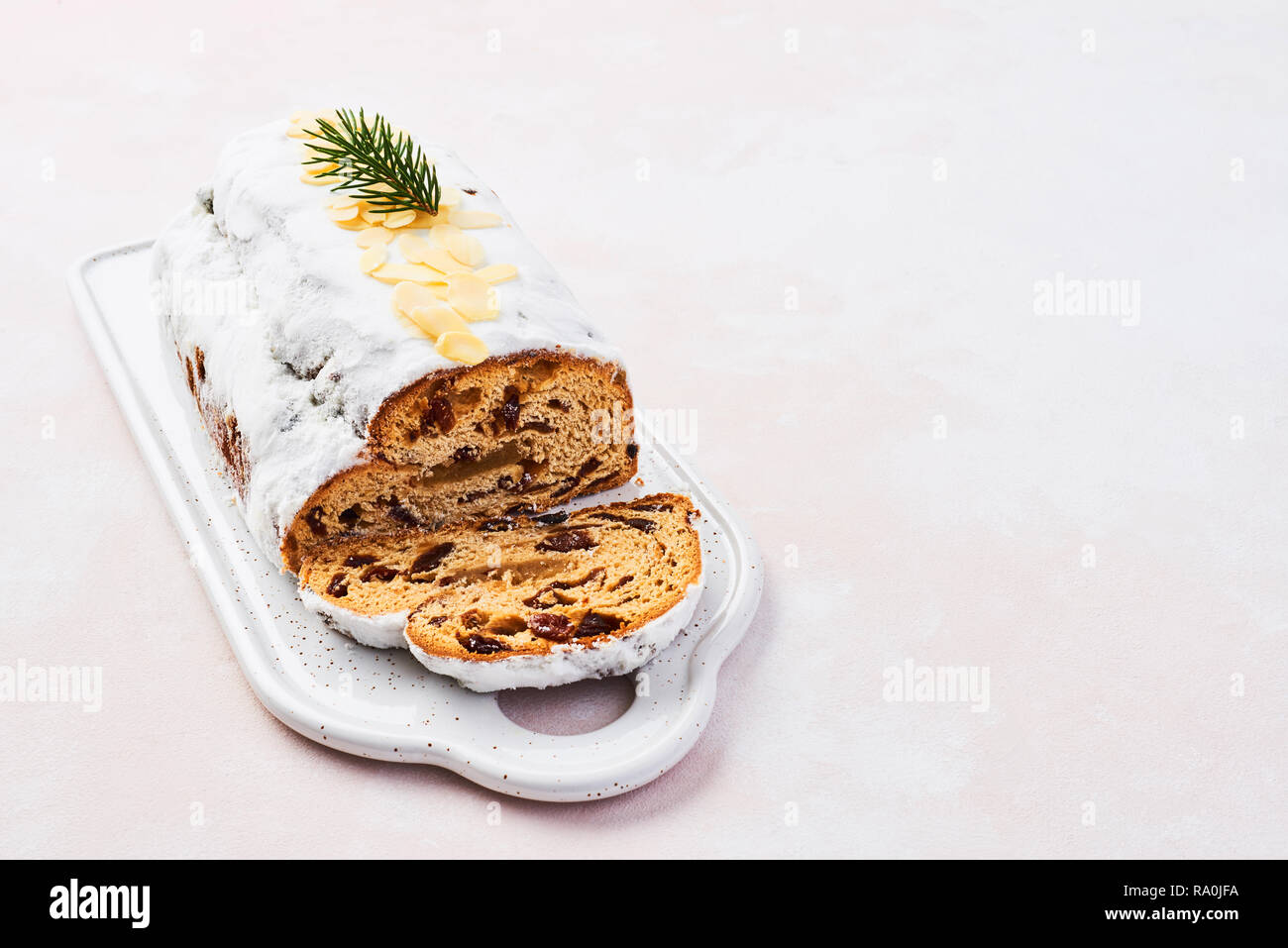 Christmas Stollen cake with icing sugar, marzipan, almonds and raisins on white serving plate. Traditional Dresdner christ pastry. Rose background wit Stock Photo