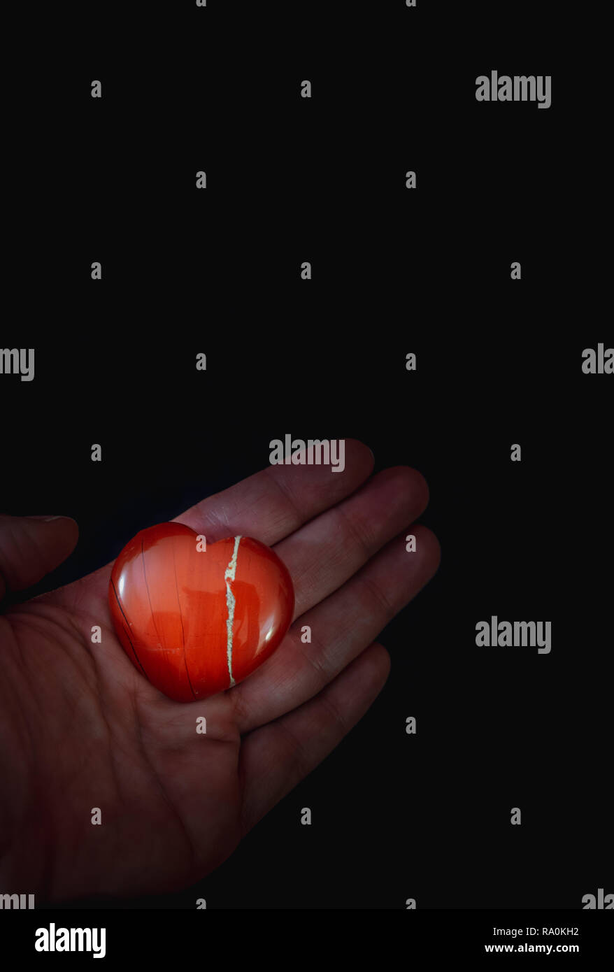 A red heart stone held in a hand against black background - love concept Stock Photo