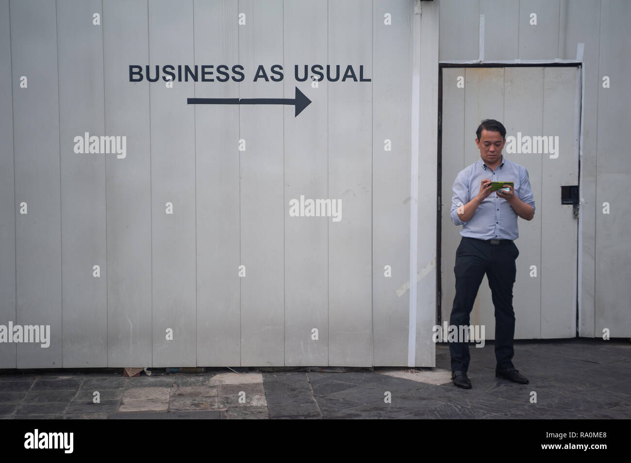 12.04.2018, Singapur, Republik Singapur, Asien - Ein Angestellter steht vor einem Baustellenzugang in Raffles City und macht eine kurze Arbeitspause.  Stock Photo