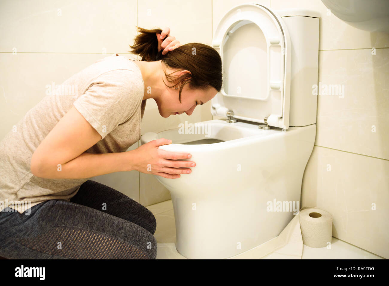 Young woman vomiting in toilet bowl at bathroom Stock Photo