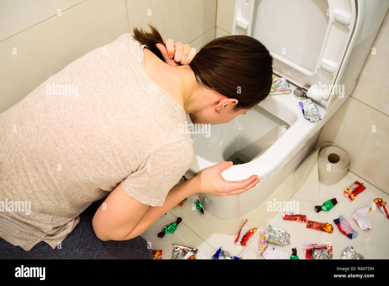 Young woman vomiting while binge eating of candies. A lot of candy wrappers on floor Stock Photo