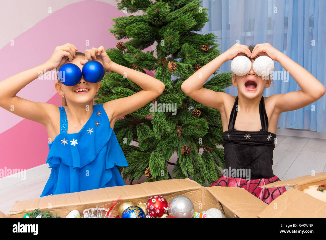 Two girls put big Christmas balls to their eyes Stock Photo