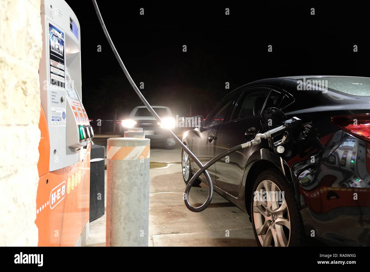 Fueling up at a gas station at night; oncoming vehicle with headlights on; gassing up; filling up the car. Stock Photo