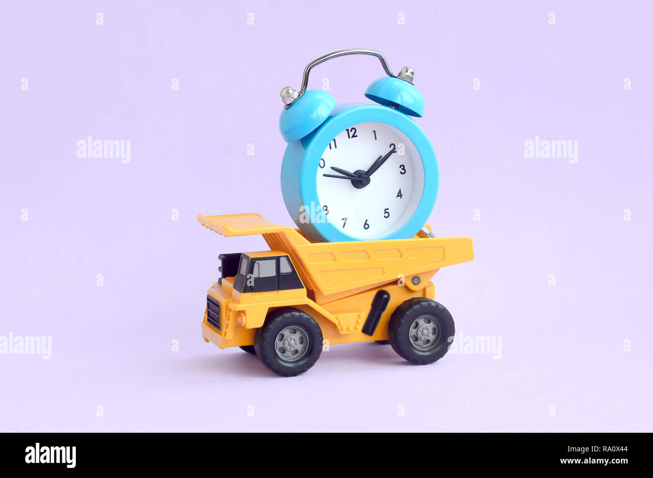 A dump truck loaded with an alarm clock on pastel lilac background. The