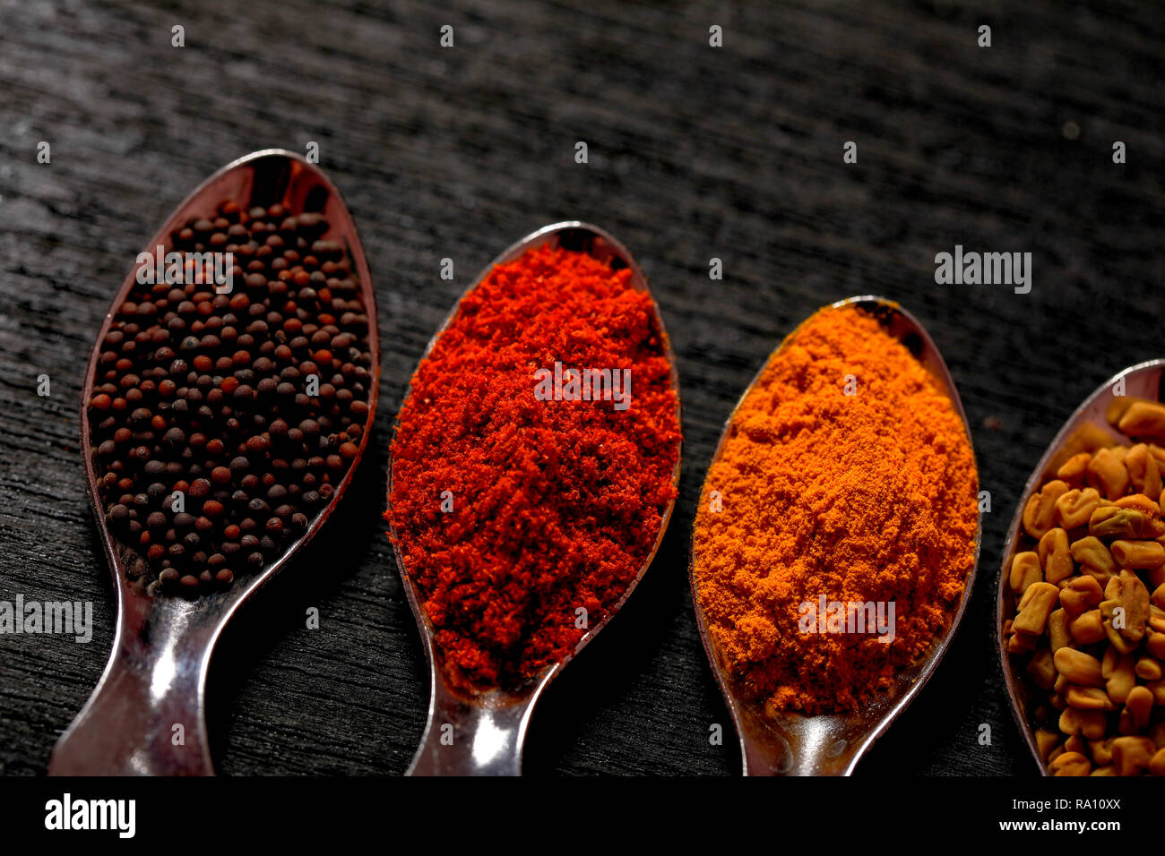 spices in spoons on black background Stock Photo