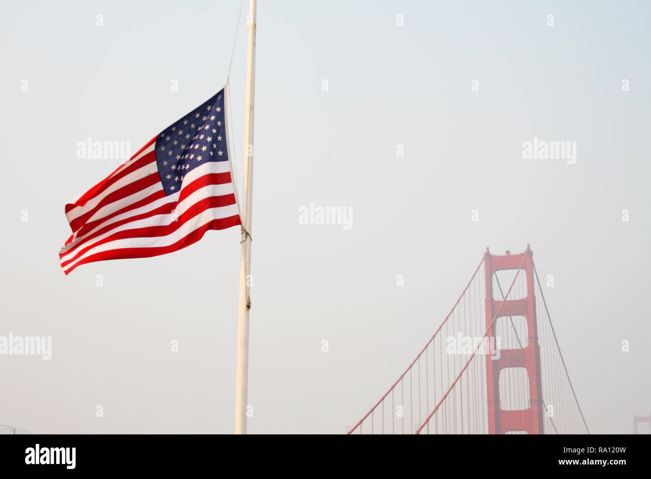 Golden Gate Bridge and US flag at half-mast, with smoke haze from November 2018 Northern Calfornia forest fires. Looking north. Stock Photo