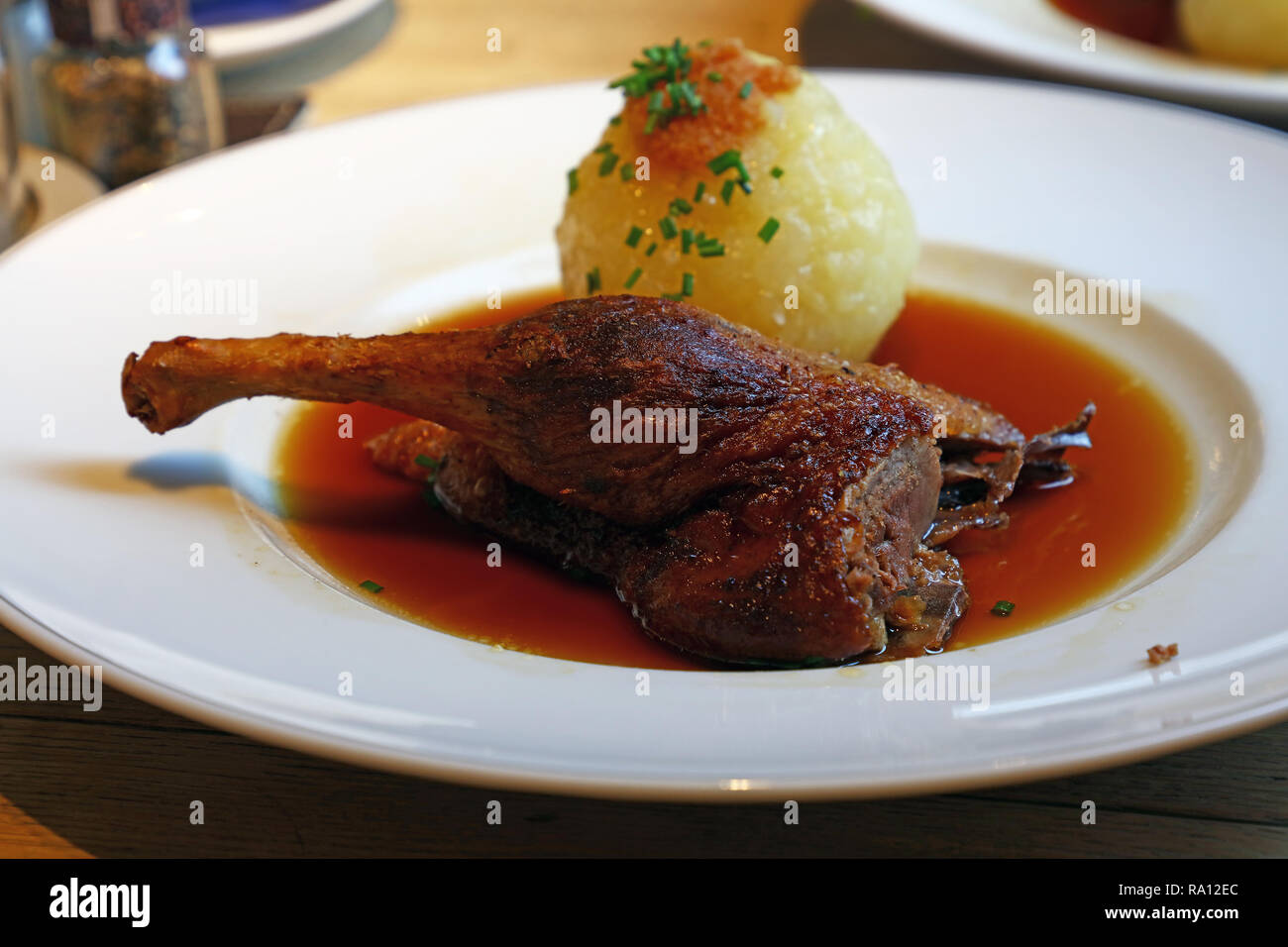 Close up portion of duck confit leg with potato dumpling ball and beer gravy, traditional dish of Bavarian German cuisine, on white plate on table, hi Stock Photo