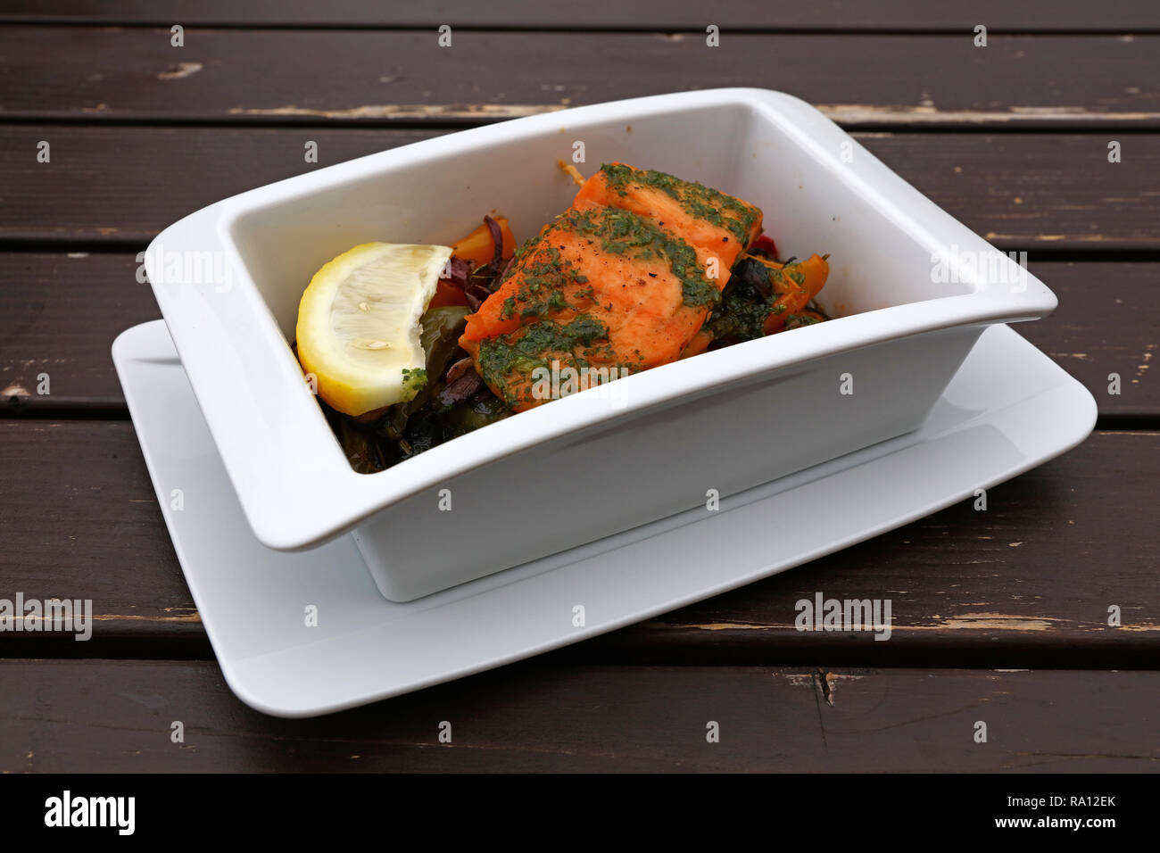 Close up portion of baked or roasted salmon with vegetables in white bowl over table, elevated top view, directly above Stock Photo