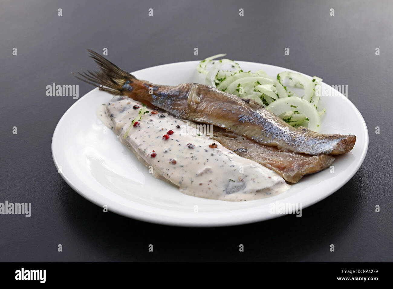Close up portion of salted pickled herring fish filets with onions and sauce on white plate over black table, high angle view Stock Photo