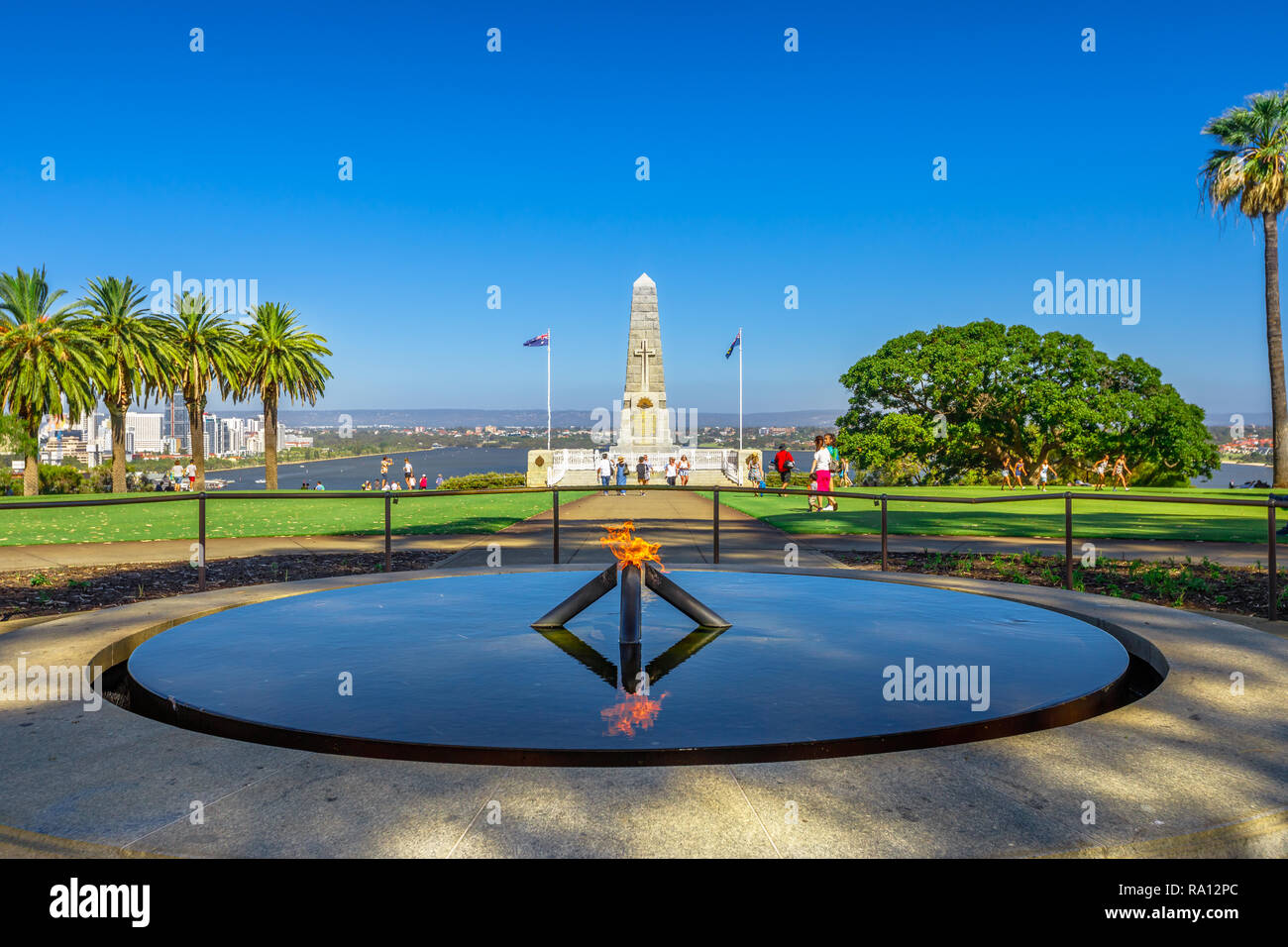 Perth, Australia - Jan 3, 2018: Eternal flame of Remembrance and Pool of Reflection with the State War Memorial behind on Mount Eliza in Kings Park. Perth cityscape on background. Copy space, blue sky Stock Photo