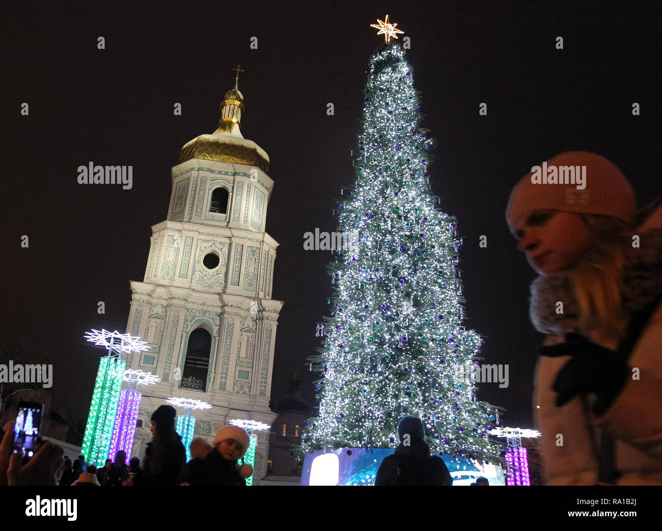 People seen next to the main Christmas tree of Ukraine, on the St. Sophia Square in Kiev, Ukraine. The main Christmas tree of Ukraine, was decorated in the northern lights style, it topped the rating of the most beautiful Christmas trees in Europe, according to the European Best Destinations website. The list included Christmas trees of 16 European. Stock Photo