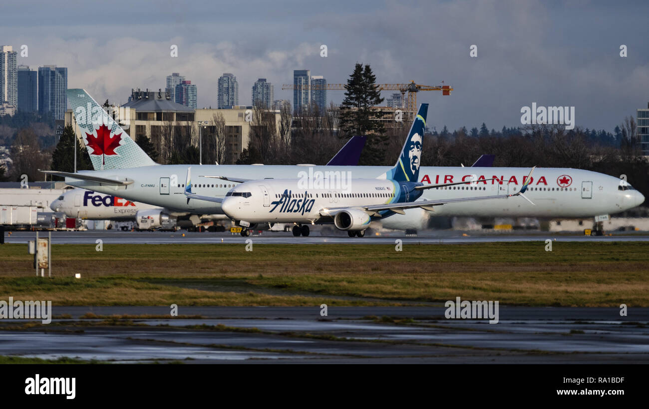 Richmond British Columbia Canada 29th Dec 2018 An Alaska Airlines Boeing 737 800 N506as Jet Airliner Takes Off From Vancouver International Airport In The Background An Air Canada Boeing 777 300er Jetliner Taxies To