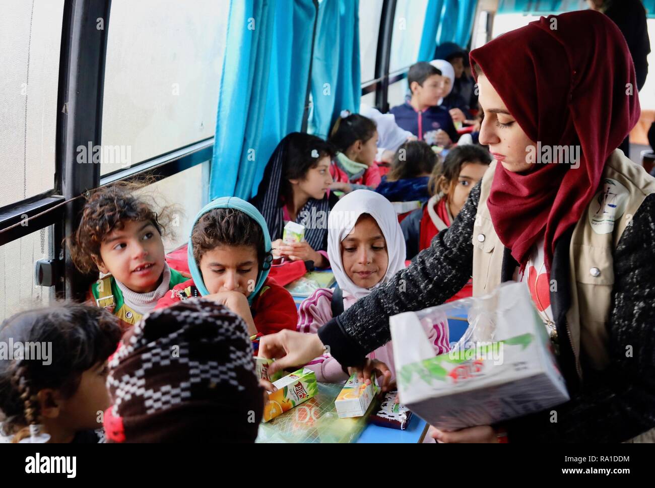 Baghdad, Iraq. 30th December 2018. A teacher hands out juice to displaced children on the 'Hope Bus' in Baghdad, capital of Iraq, on Dec. 27, 2018.    At a forgotten slum in the southeast of Baghdad, capital of Iraq, a glimmer of hope shines in the hearts and minds of dozens of internal displaced children as a nongovernmental organization (NGO) turned a large old bus into a mobile school. Credit: Xinhua/Alamy Live News Stock Photo