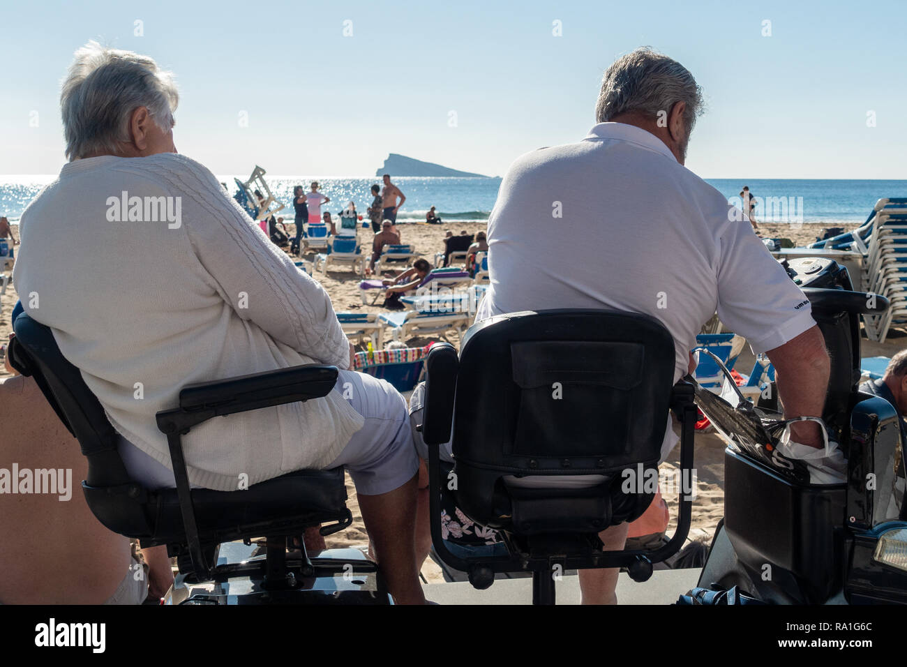 Benidorm, Spain. 30 December 2018. British tourists mix with locals on the beaches and in the bars and restaurants as they escape the cold British weather and head south to Spain. High temperatures meant that the beaches were busy from early morning with families enjoying the calm sea and temps of about 17 Celsius. middle aged couple sitting an a disability scooter on the promenade in this popular Spanish resort. Credit: Mick Flynn/Alamy Live News Stock Photo