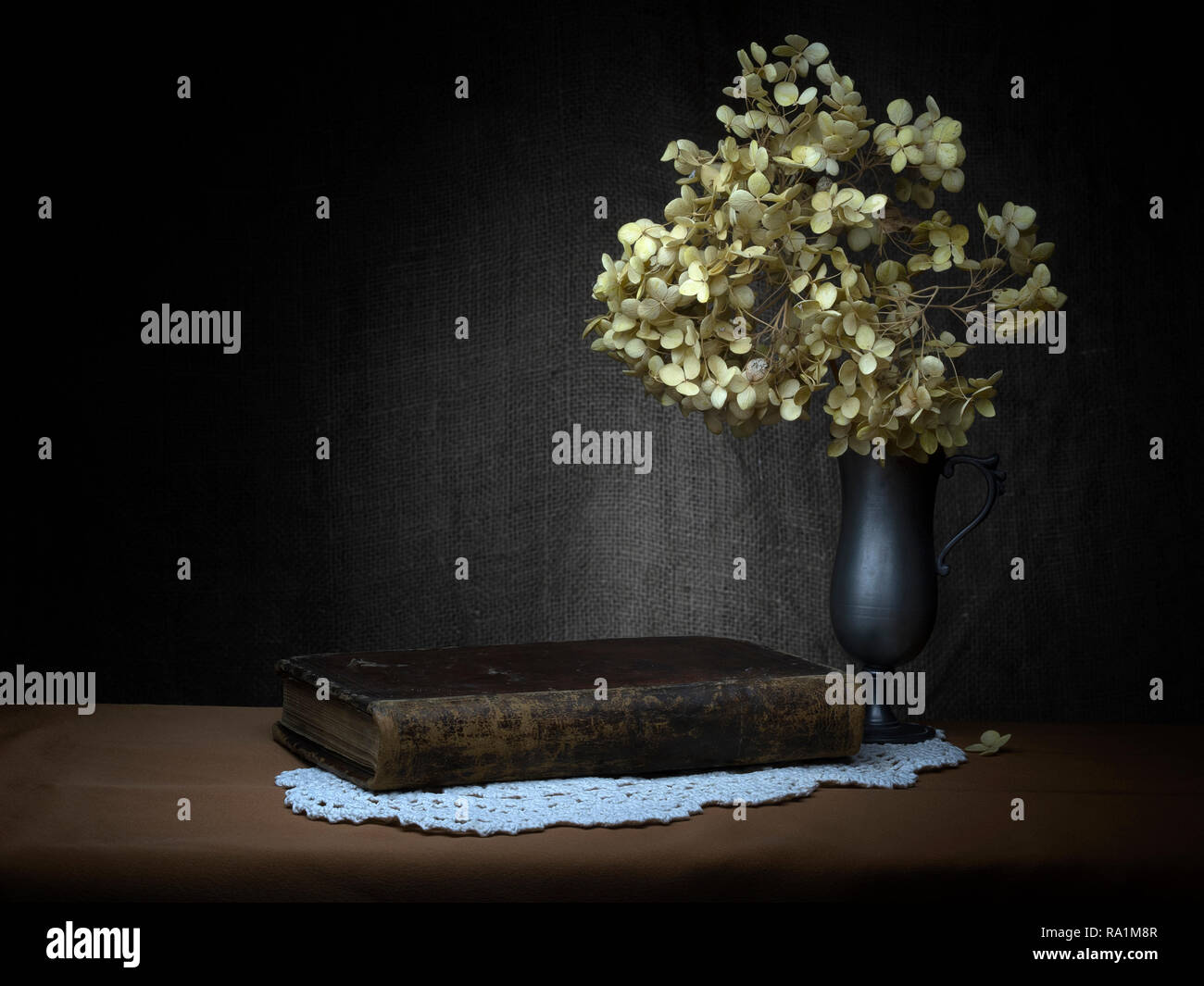 Melancholy, still life with old book, dried hydrangea flowers. Baroque, chiaroscuro style by means of light painting. Stock Photo