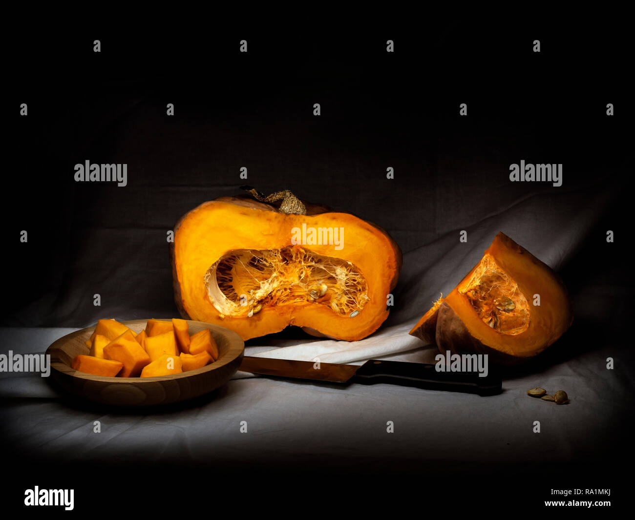 Acorn winter squash, pumpkin, prepared for cooking, cubes with seeds, knife. Chiaroscuro, baroque style light painting. Stock Photo