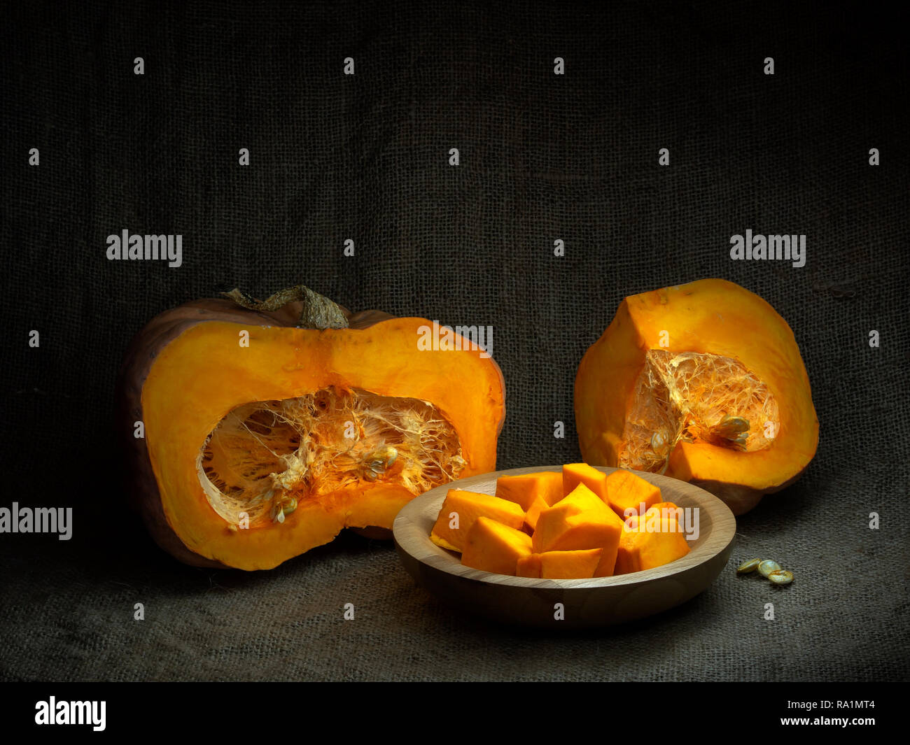 Acorn winter squash, pumpkin, prepared for cooking, cubes with seeds. Life cycle concept. Chiaroscuro, baroque style light painting. Stock Photo