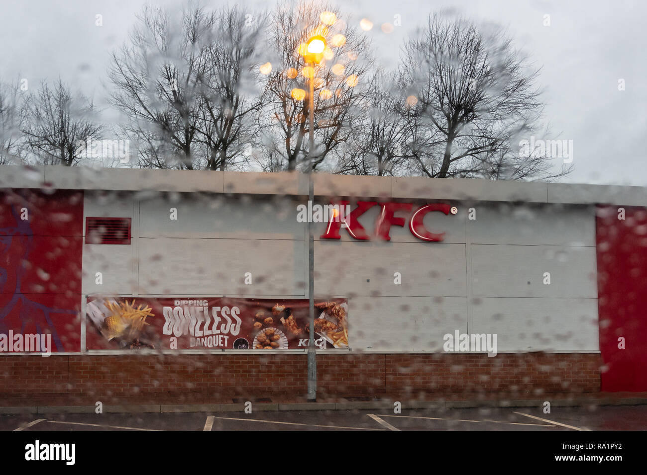 Theside of a KFC outlet seen through a blurry rain spattered car window with the focus on KFC, with a dreary dull wet winter background Stock Photo