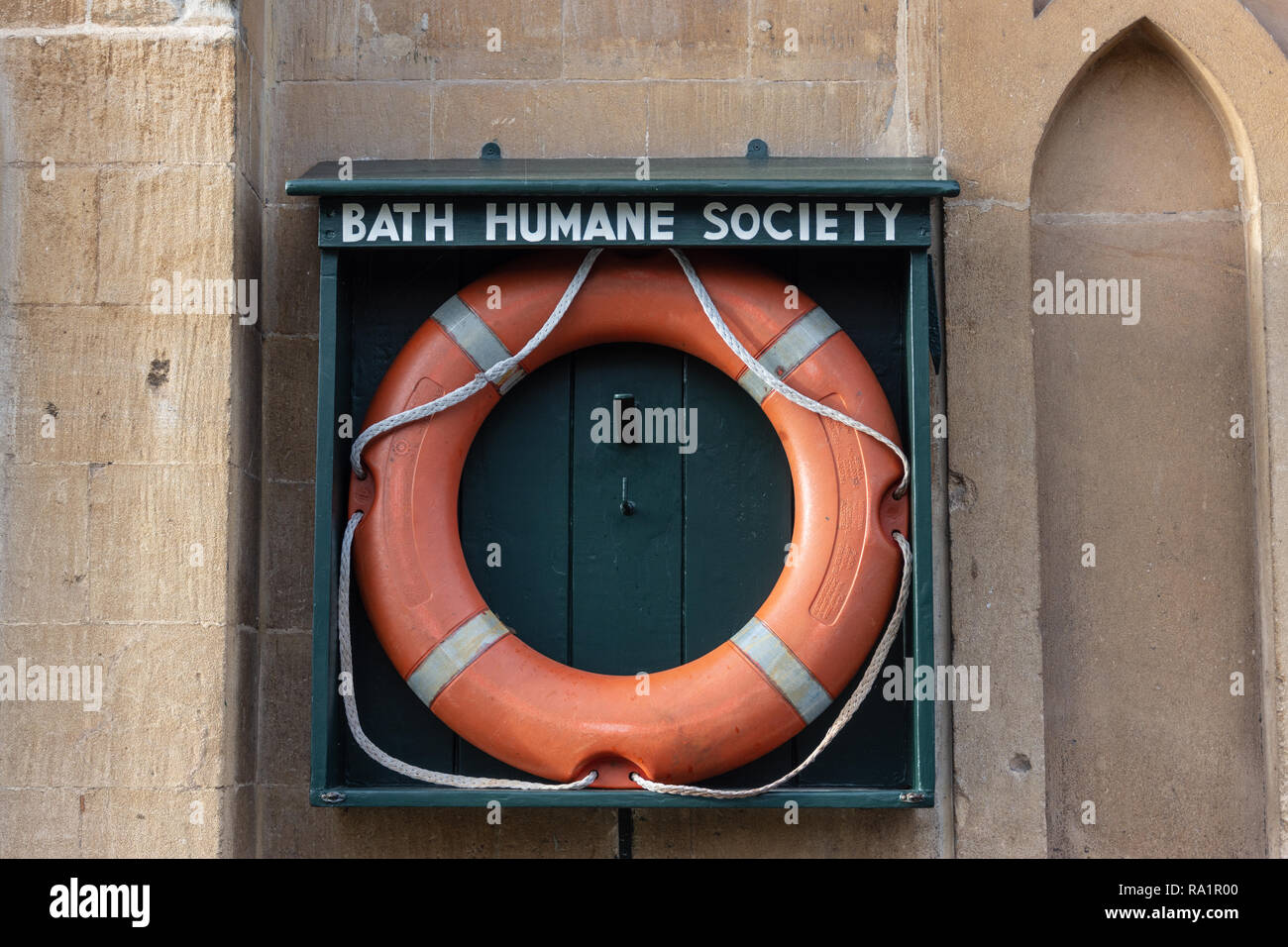 An orange life preserver in an open wooden holder marked 'Bath Humane Society' on a wall next to the Kennet and Avon canal in Bath Somerset UK Stock Photo