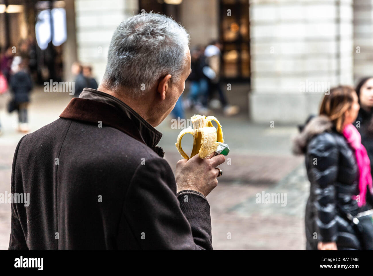 Rear view of a man eating a banana on James street, Covent Garden, London, England UK. Stock Photo