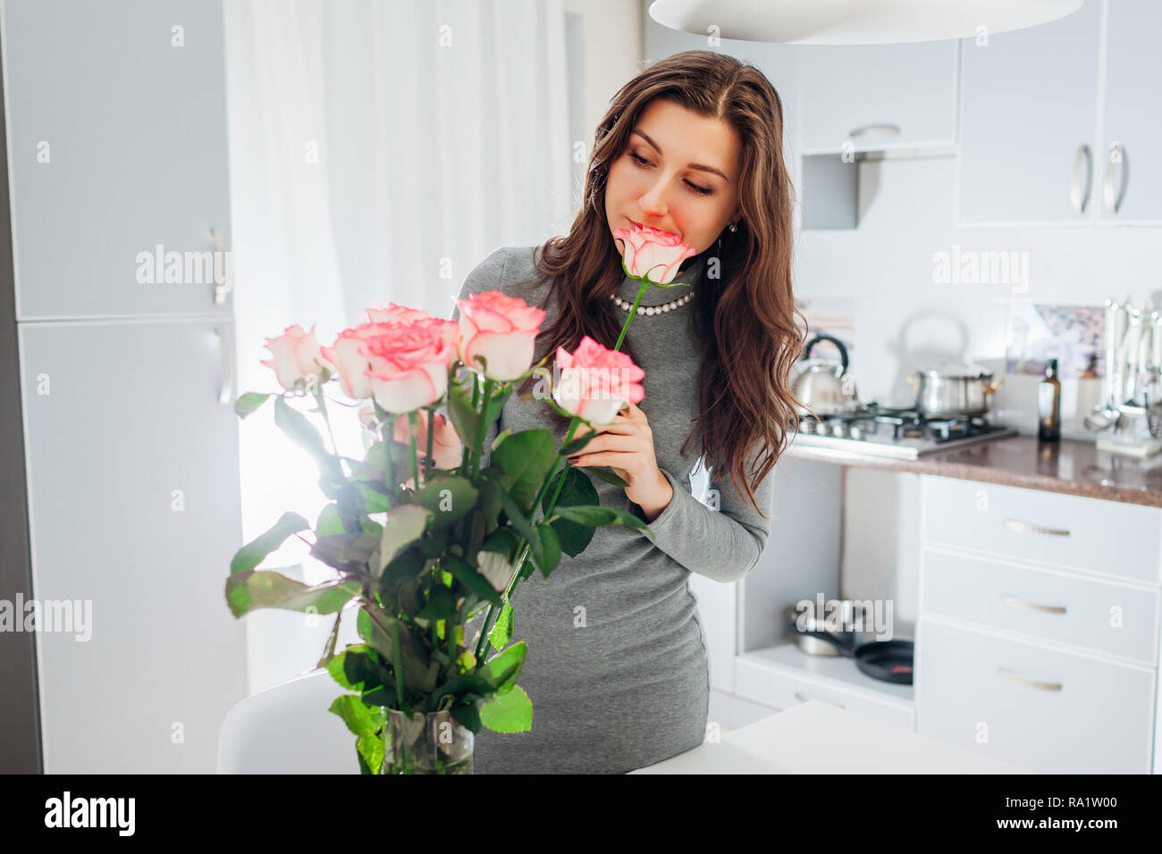 Woman puts pink roses in vase smelling flower. Young housewife taking