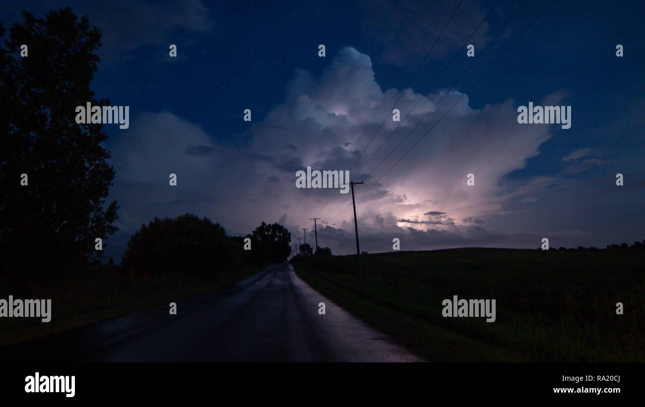 A storm cloud releases a flash of lightning over a dark country road. Stock Photo