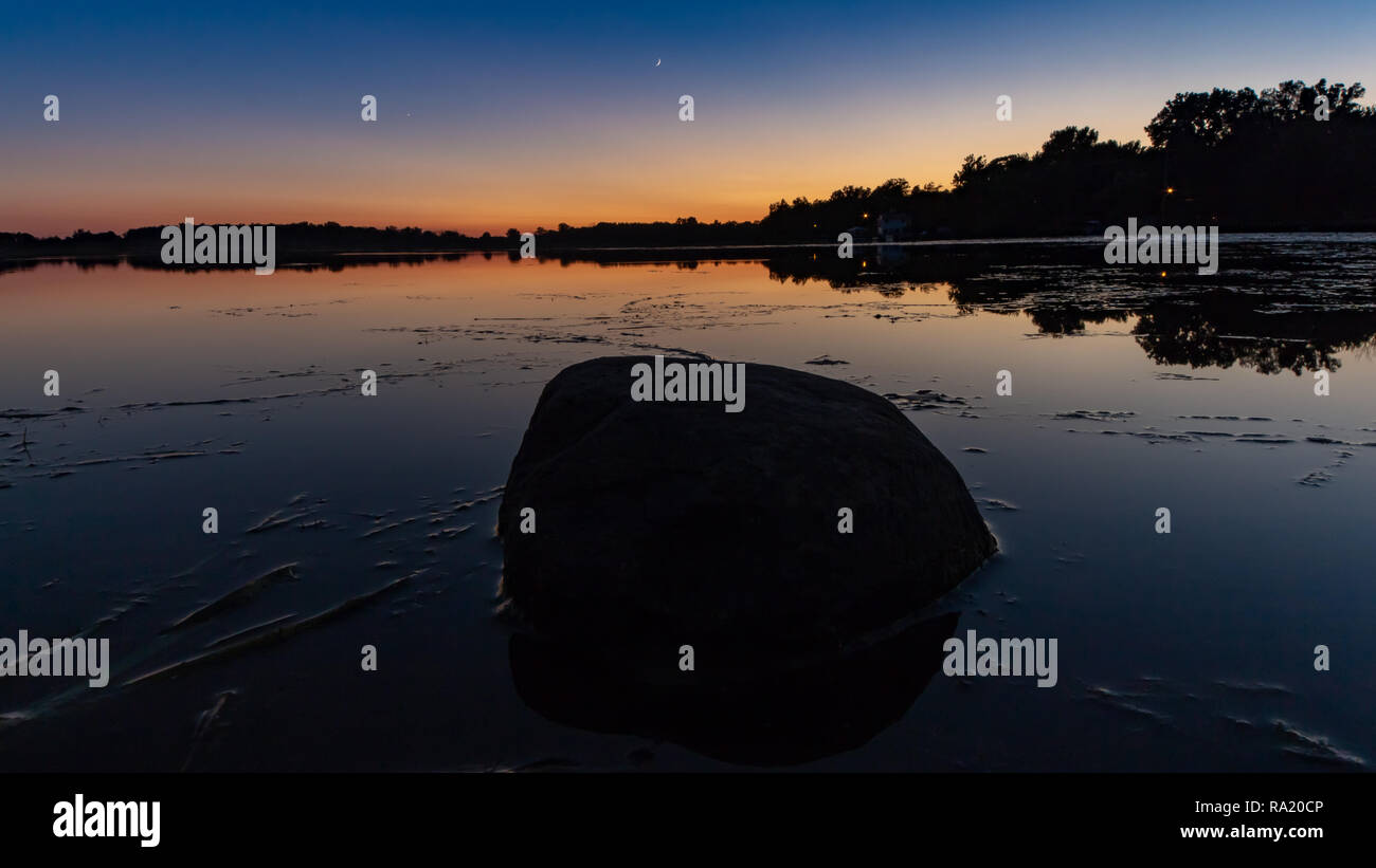 A solitary stone sits in the reflection of the sunset sky. Stock Photo