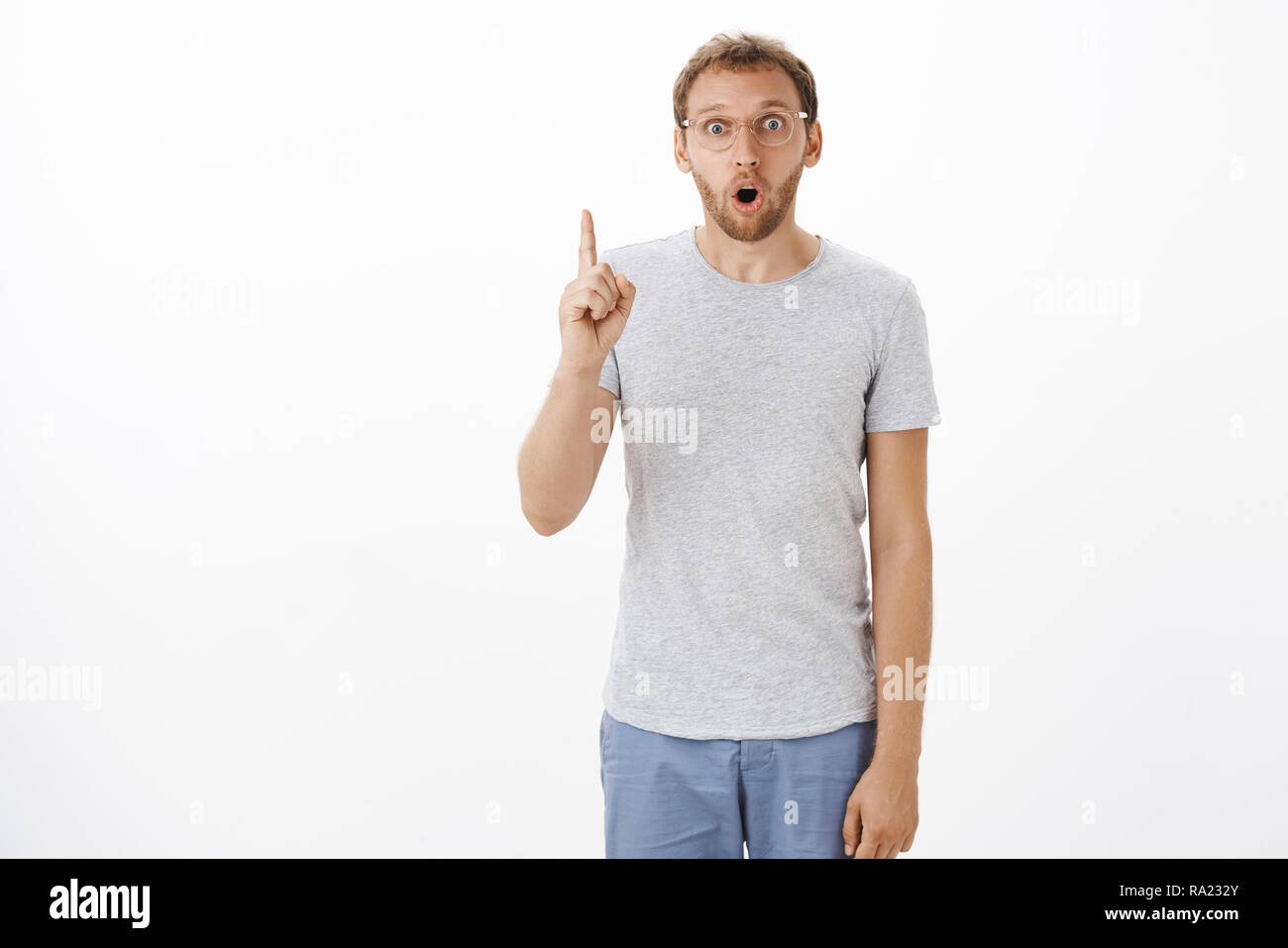 Got excellent idea listen. Stunned excited charming mature guy with bristle gasping opening mouth in surprise while making up great plan raising index finger in eureka gesture over white wall Stock Photo