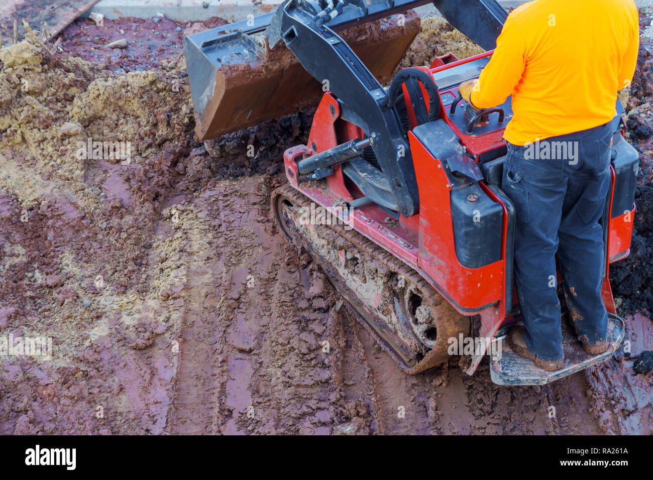 Excavation works at the construction site. Bulldozer or a backhoe loader dumping ground into the level the ground near the house Stock Photo