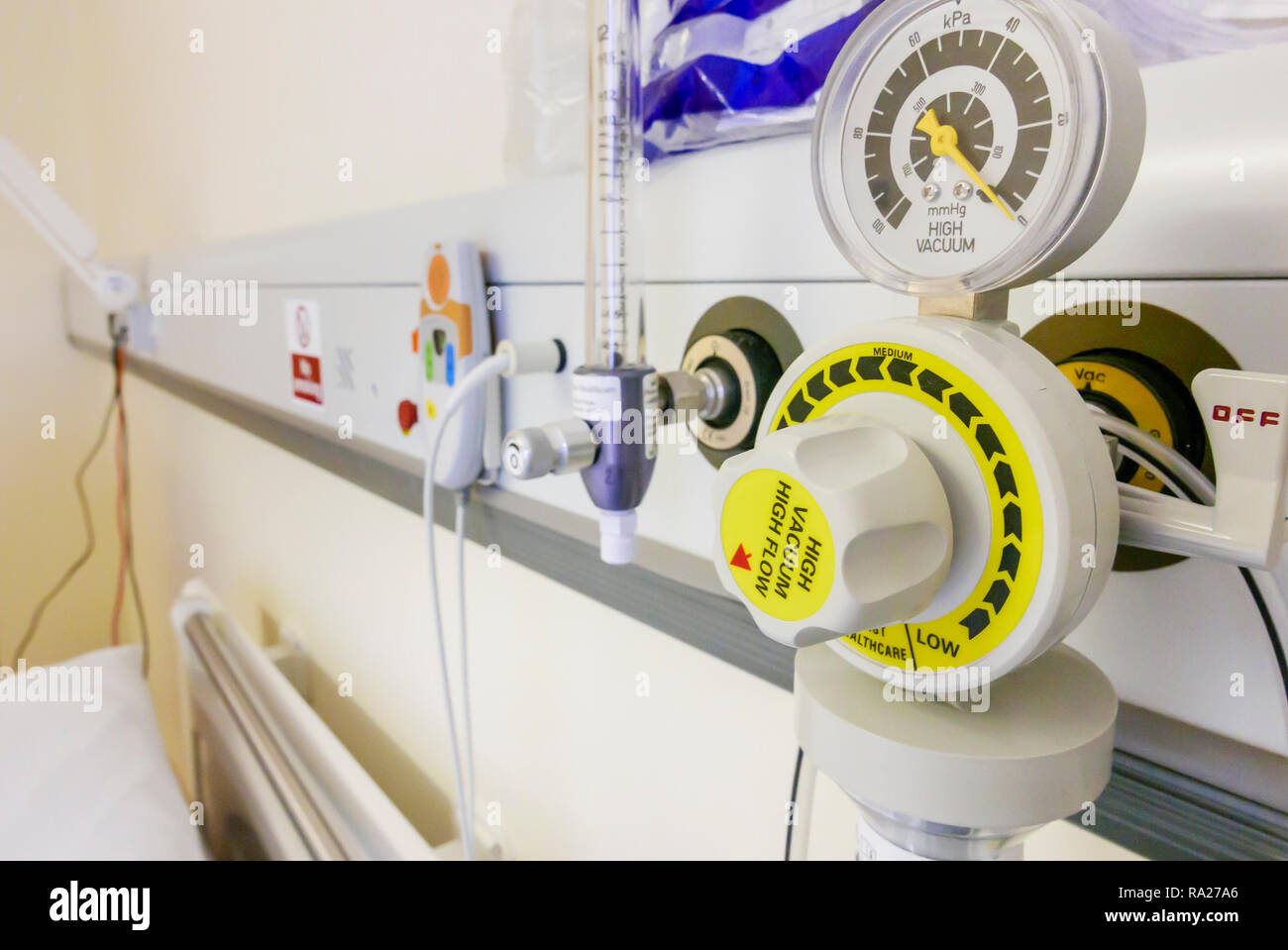 Bed head unit in a hospital ward showing a suction vacuum pressure gauge, an oxygen supply and a nurses call bell. Stock Photo