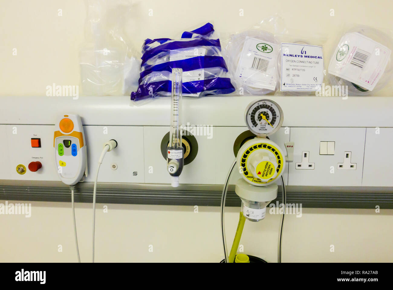 Bed head unit in a hospital ward showing a suction vacuum pressure gauge, an oxygen supply and a nurses call bell. Stock Photo