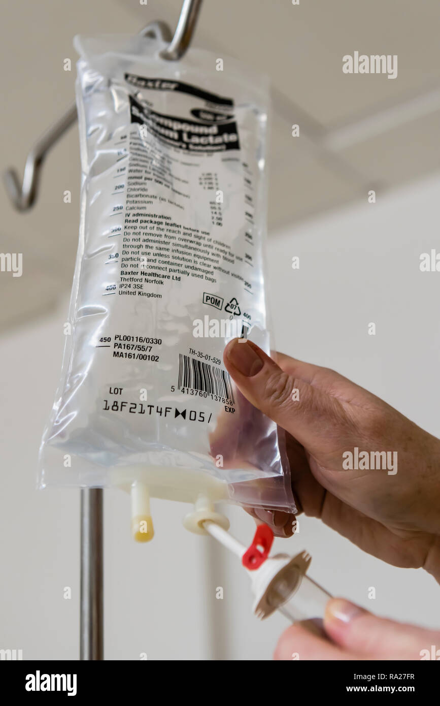Nurse attaches a giving set to a bag of saline to administer to a patient in a hospital ward. Stock Photo