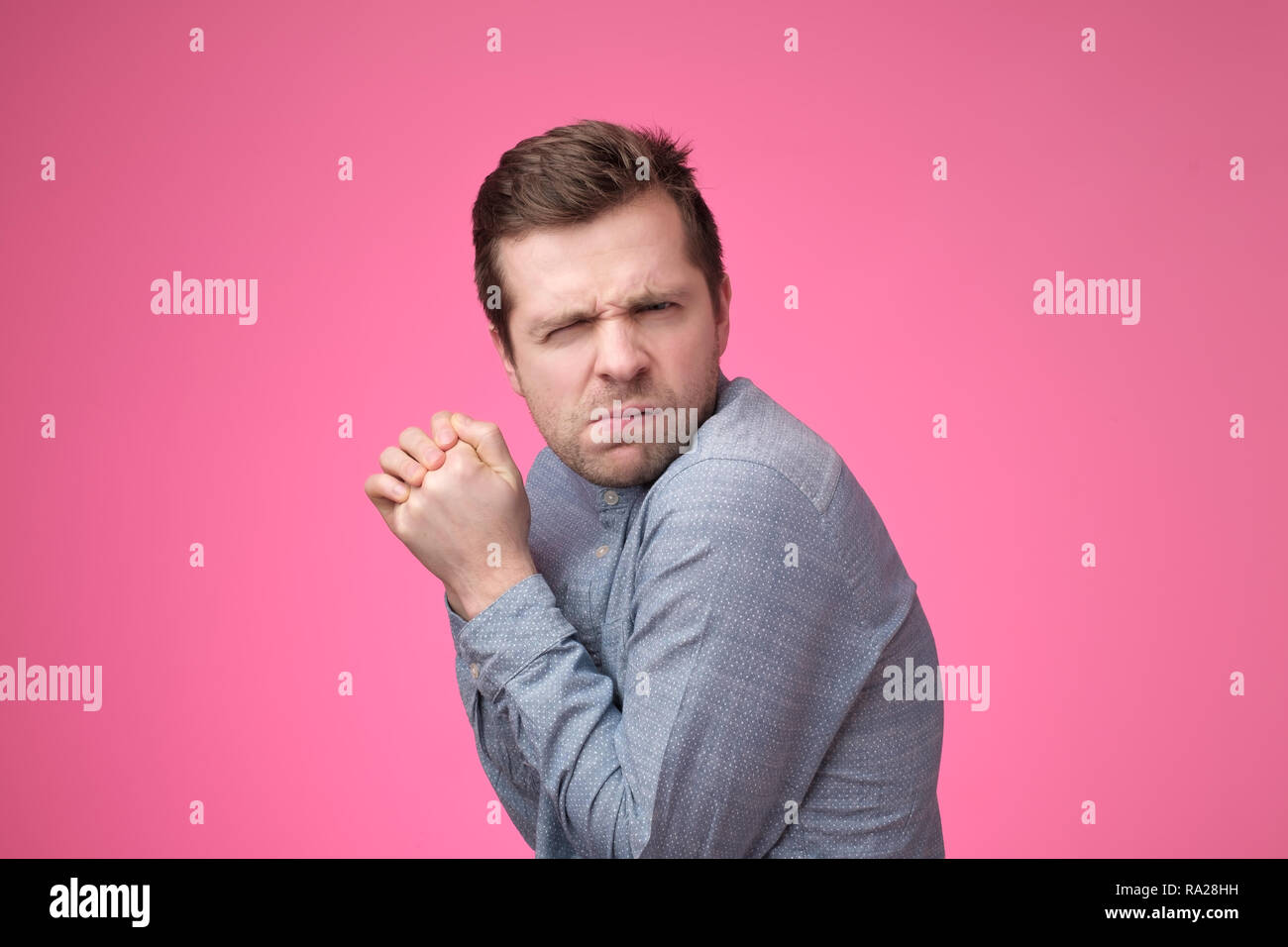 A young greedy man hides something in his hands and looks warily forward. Stock Photo