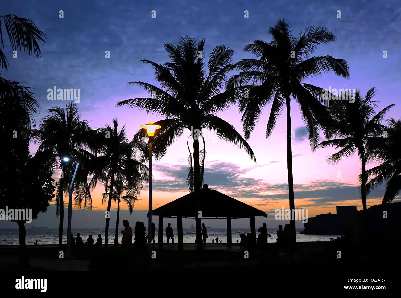 Tropical beach scene with palm trees at dusk with people as silhouettes Stock Photo